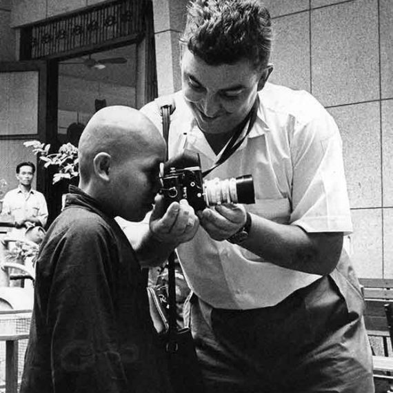 Faas demonstrates his camera for a Buddhist monk, Saigon, 1962